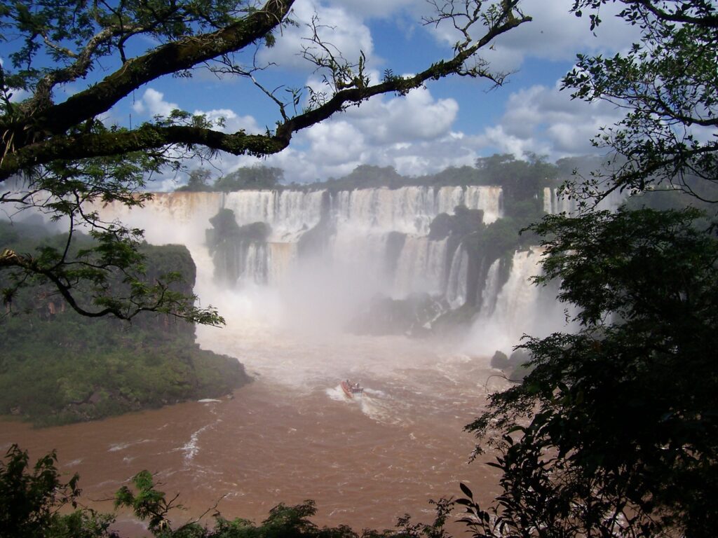 Kleines Ausflugsboot auf dem Fluss unterhalb der tosenden Iguazú-Fälle, umrahmt von Ästen, Argentinien
