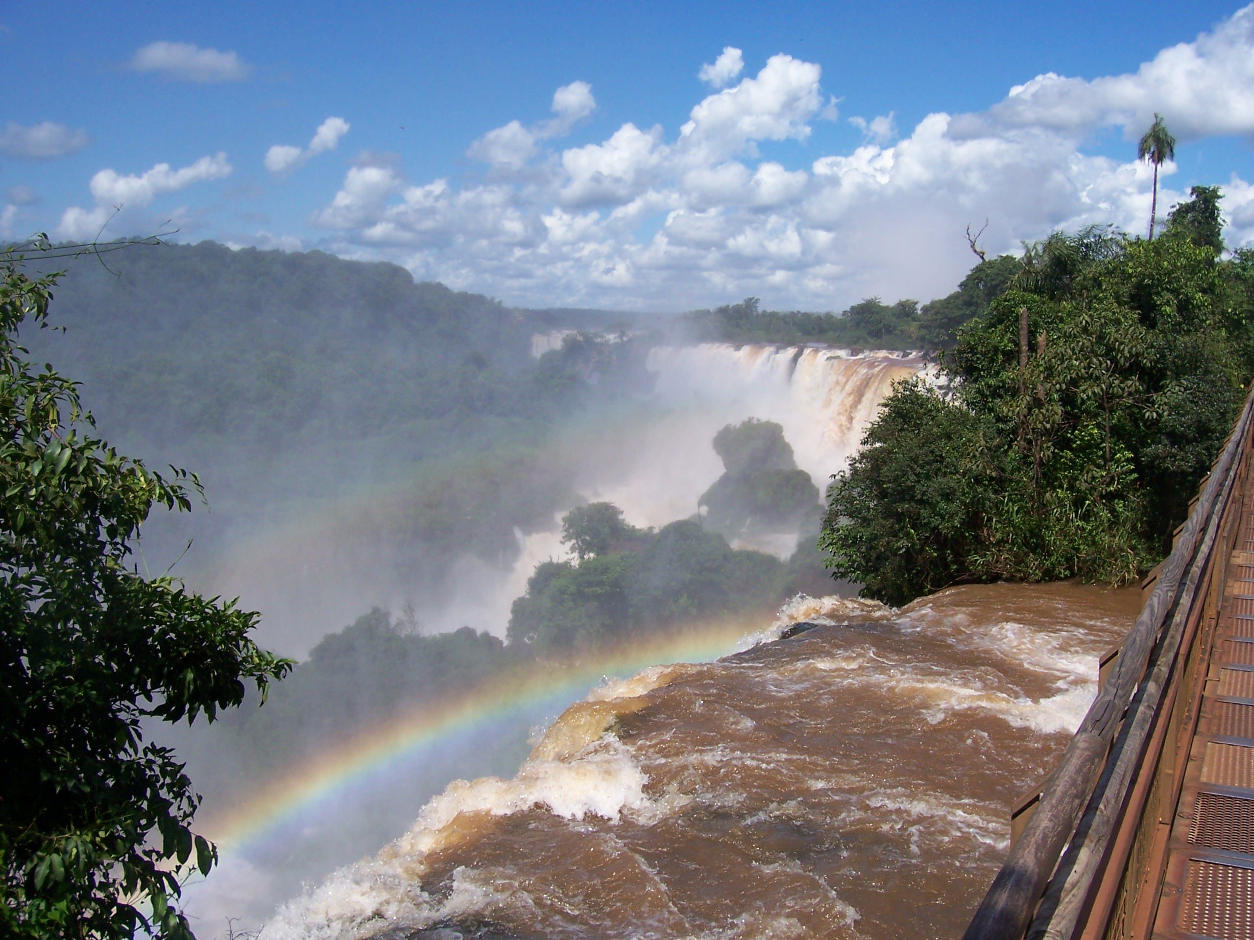 Regenbogen über den tosenden Iguaçu-Fällen, gesehen von einem Holzsteg aus, Brasilien