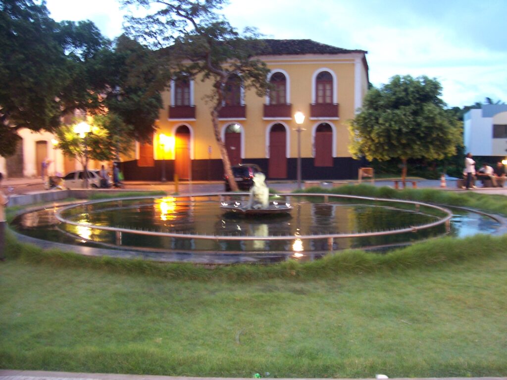 Beleuchteter Brunnen mit Statue vor einem gelben Kolonialhaus bei Dämmerung in São Luís, Brasilien