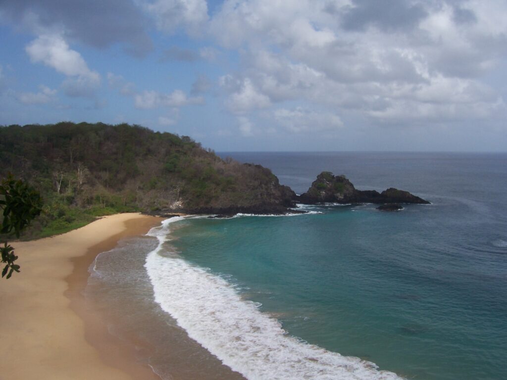 Luftaufnahme einer geschwungenen Sandbucht mit türkisfarbenem Wasser und Felsen auf Fernando de Noronha, Brasilien