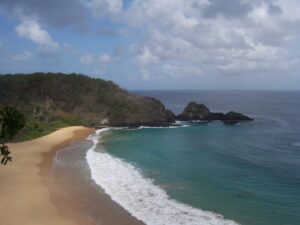 Luftaufnahme einer geschwungenen Sandbucht mit türkisfarbenem Wasser und Felsen auf Fernando de Noronha, Brasilien