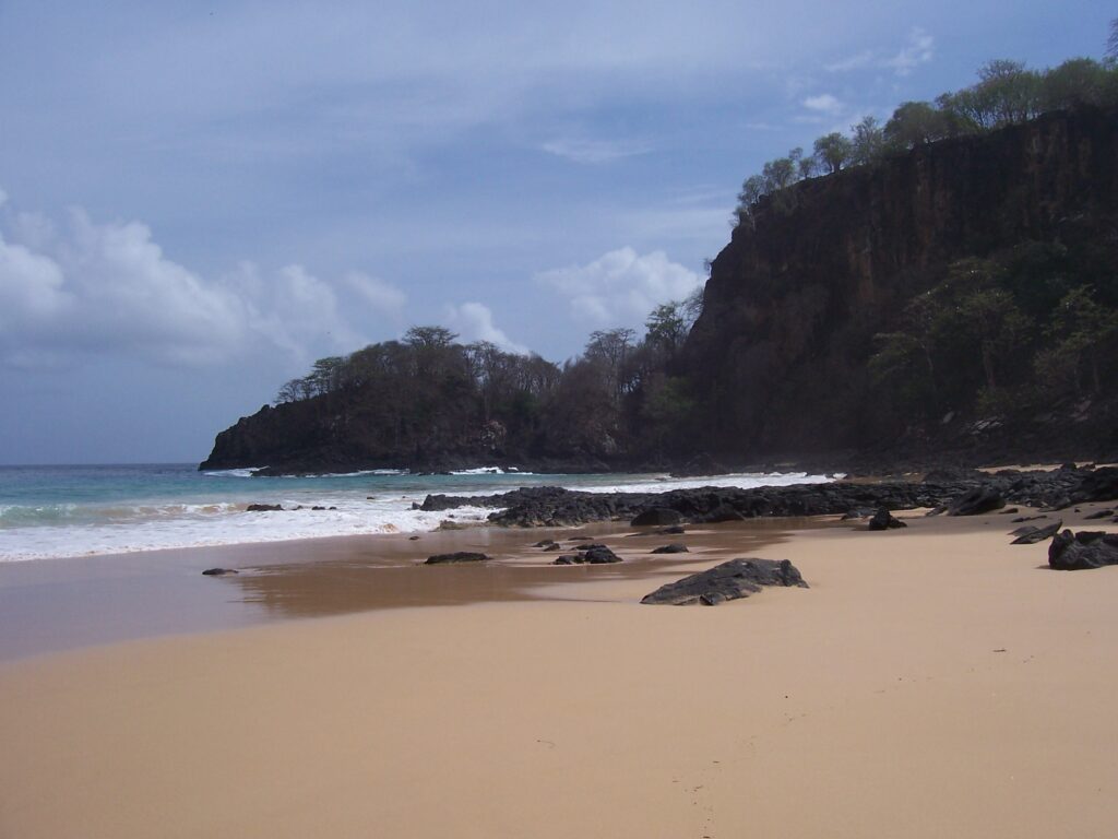 Einsamer Sandstrand mit dunkler Basaltklippe und türkisfarbenem Meer auf Fernando de Noronha, Brasilien