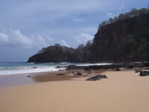 Einsamer Sandstrand mit dunkler Basaltklippe und türkisfarbenem Meer auf Fernando de Noronha, Brasilien