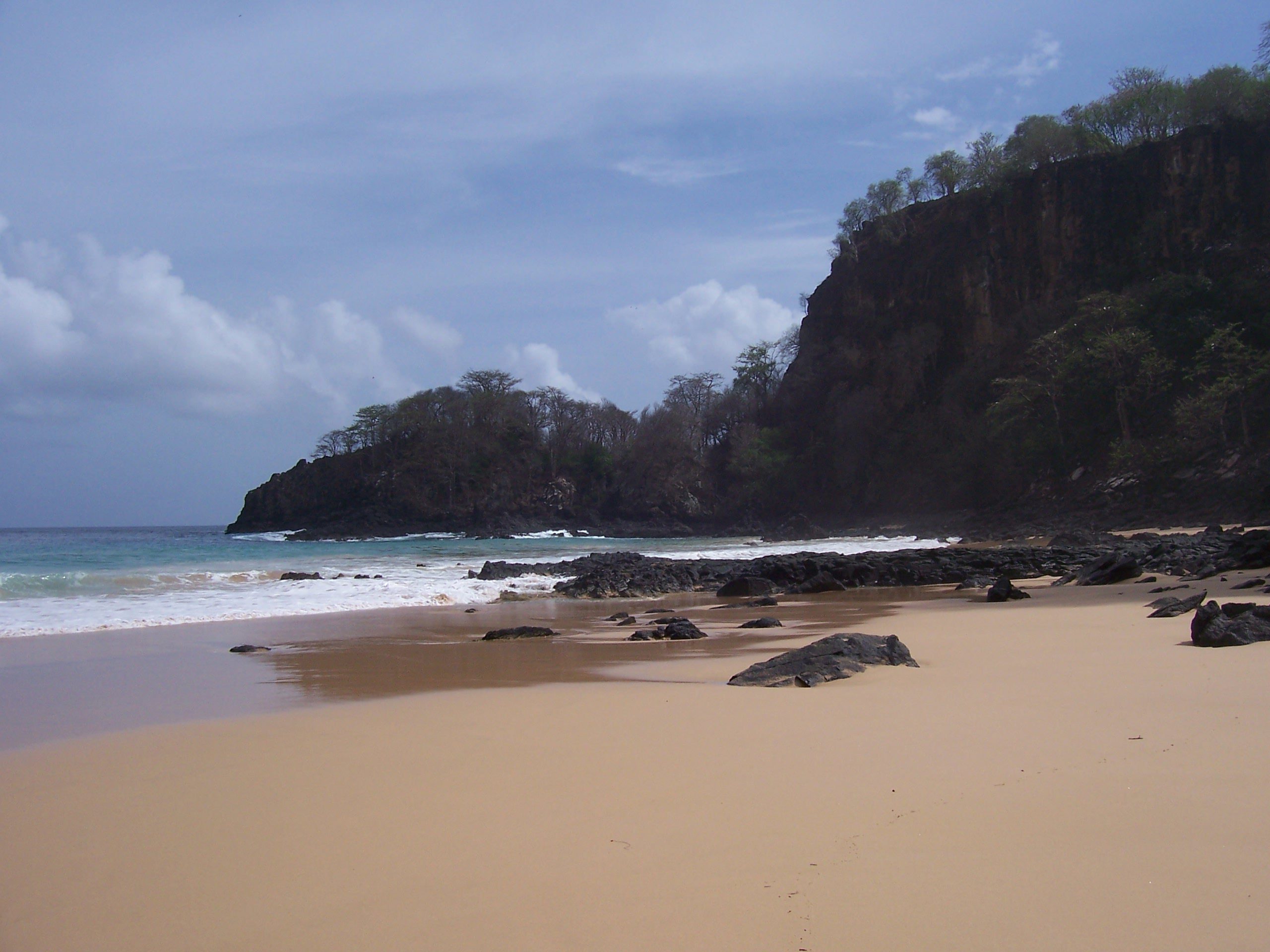 Einsamer Sandstrand mit dunkler Basaltklippe und türkisfarbenem Meer auf Fernando de Noronha, Brasilien