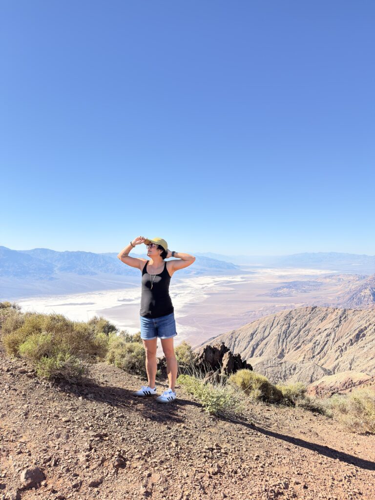 Frau mit Kappe blickt bei Sonnenschein auf die Salzebene des Death Valley vom Dante's View aus