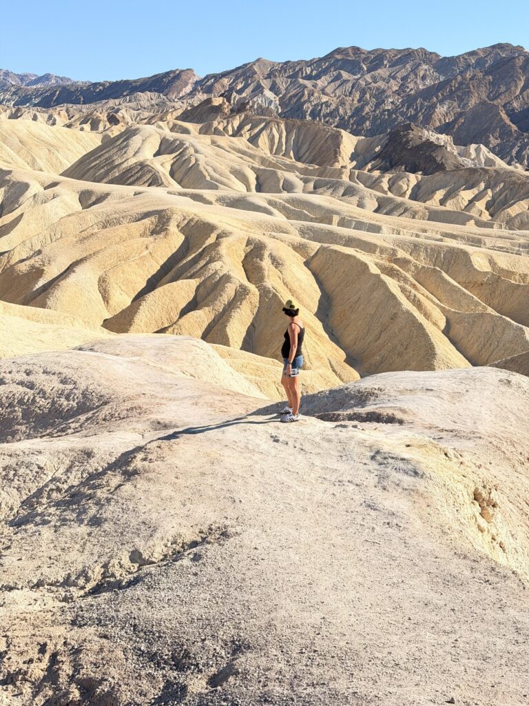 Frau steht auf einem hellen Felsen und blickt auf die goldenen, erodierten Badlands von Zabriskie Point