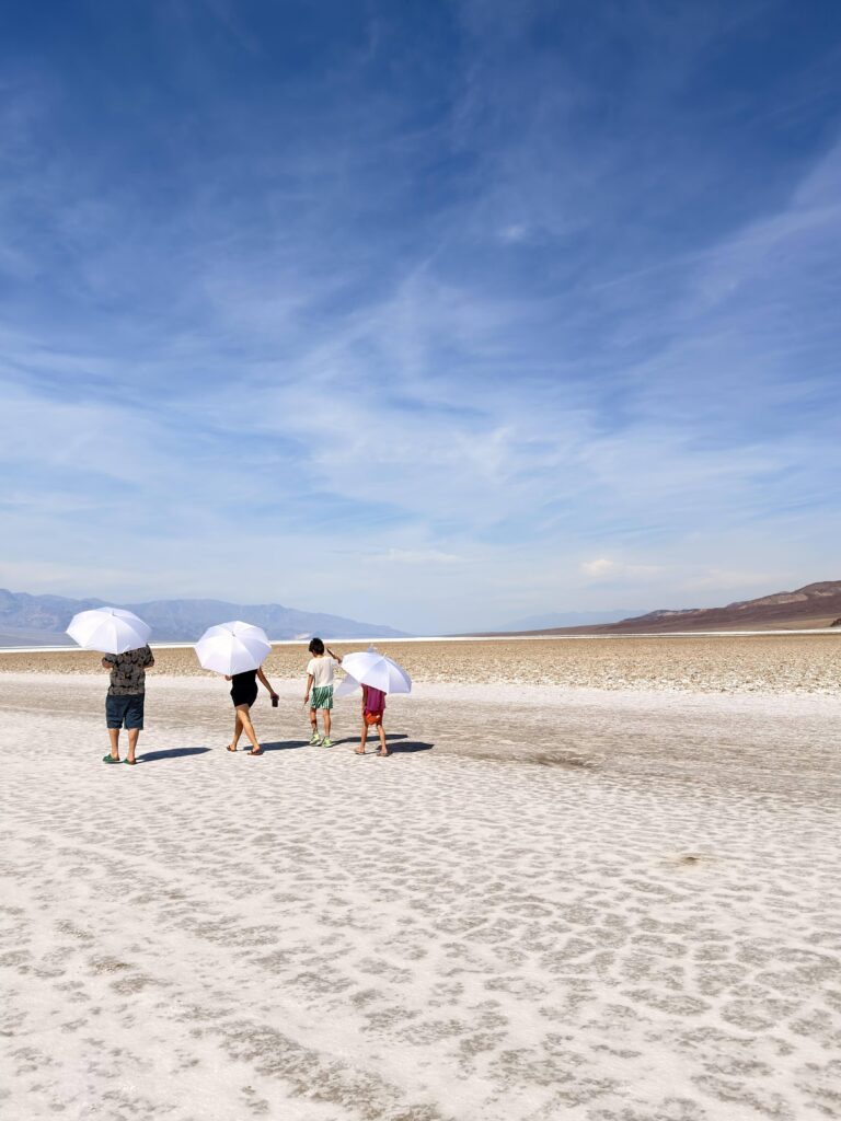 Familie mit weißen Sonnenschirmen läuft über die Salzkruste von Badwater Basin
