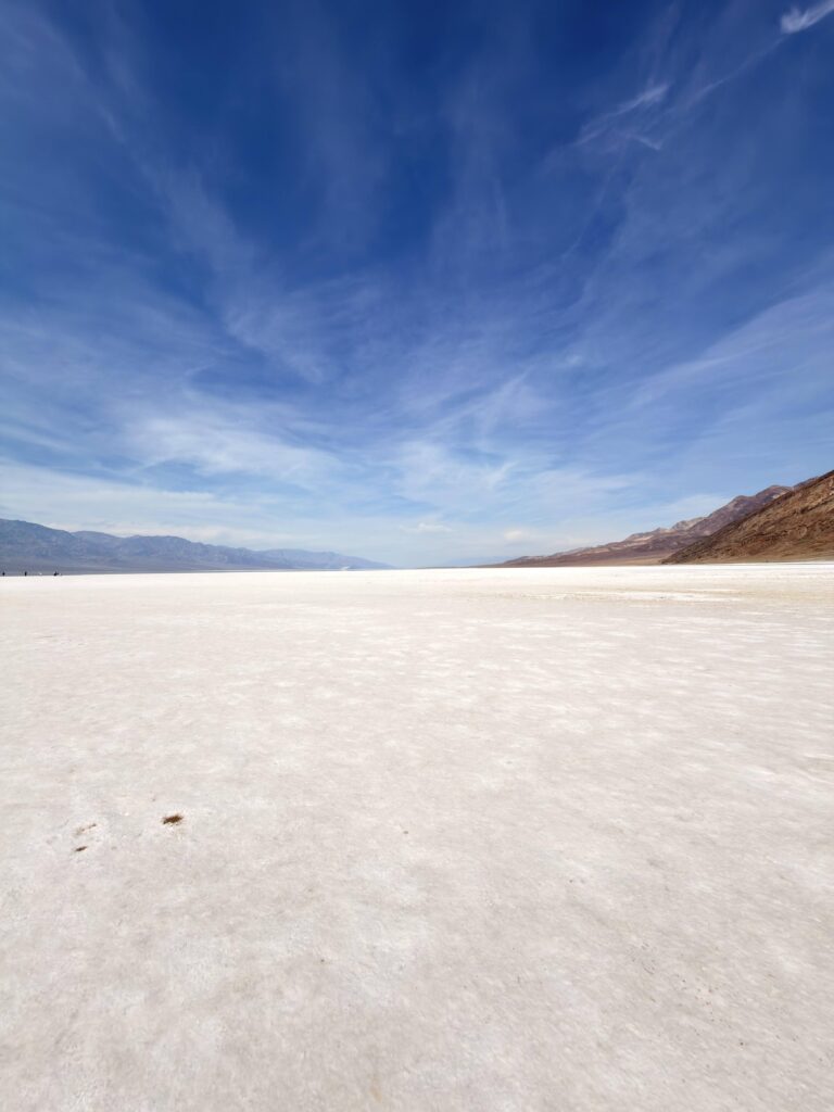 Weite, weiße Salzebene von Badwater Basin unter blauem Himmel mit Wolkenschleiern