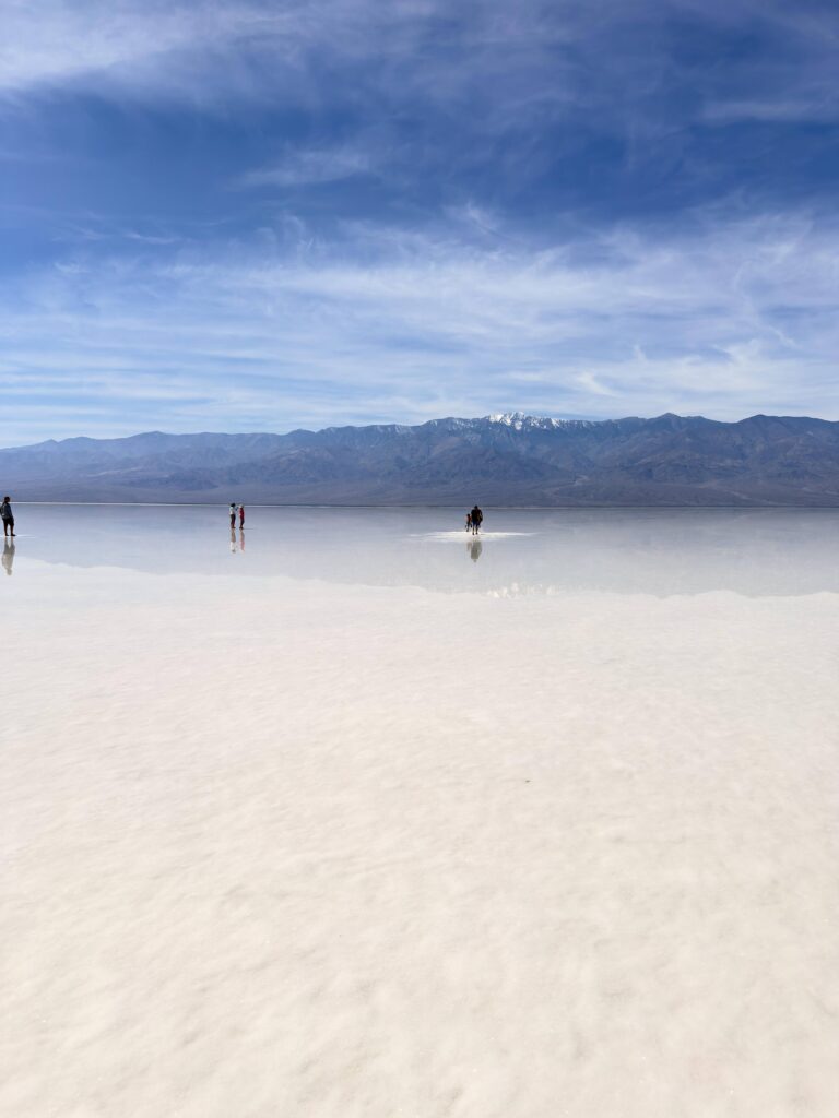 Menschen laufen über eine spiegelnde Wasserfläche auf der Salzebene von Badwater Basin