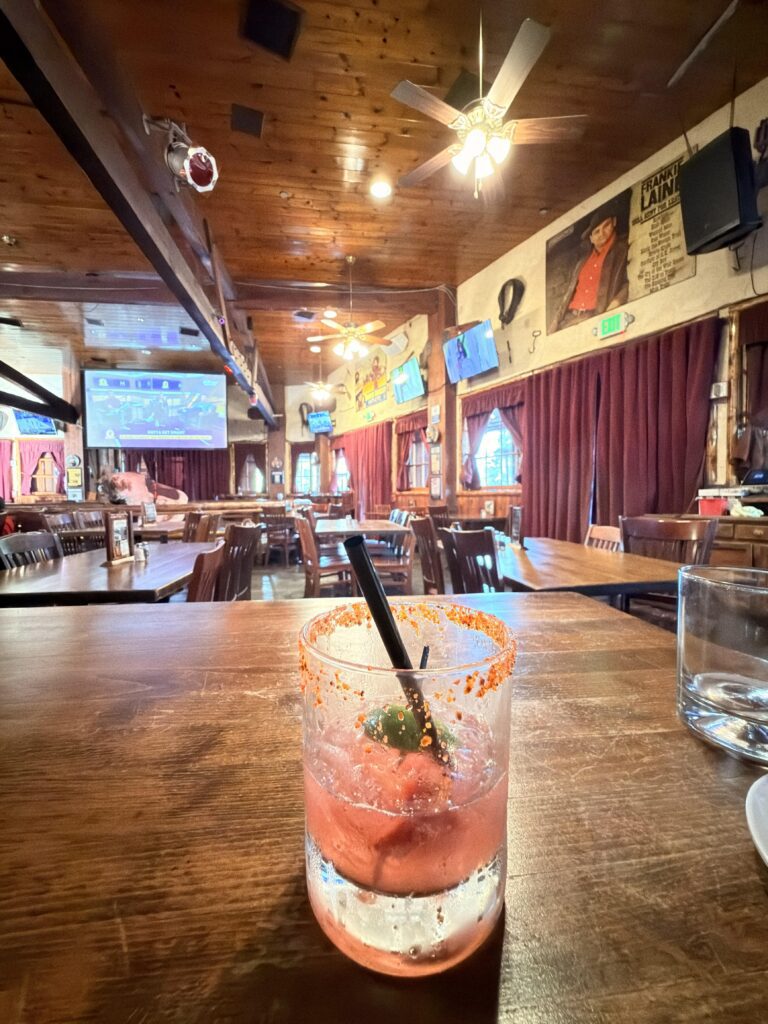 Cocktail mit Chili-Salzrand und Limette auf einem Holztisch im Saddle Ranch Restaurant
