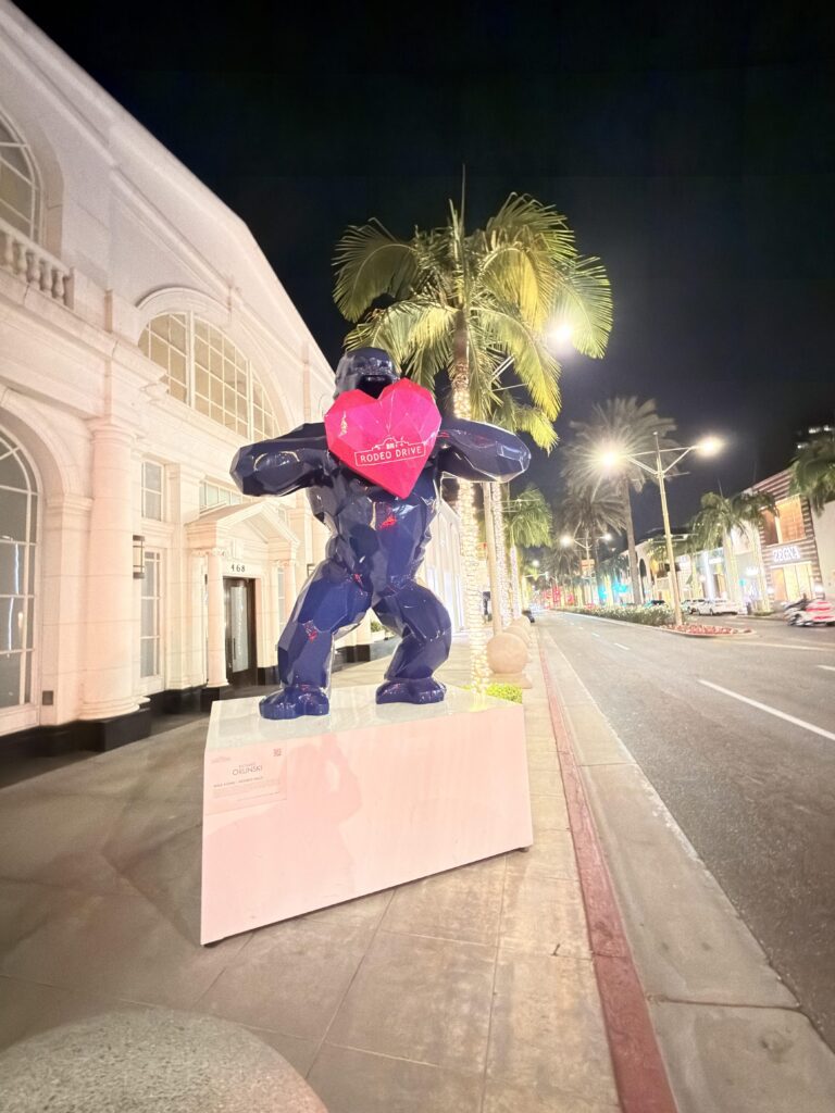 Dunkelblaue Gorilla-Skulptur mit pinkem Herz auf der Rodeo Drive in Beverly Hills, umgeben von Palmen