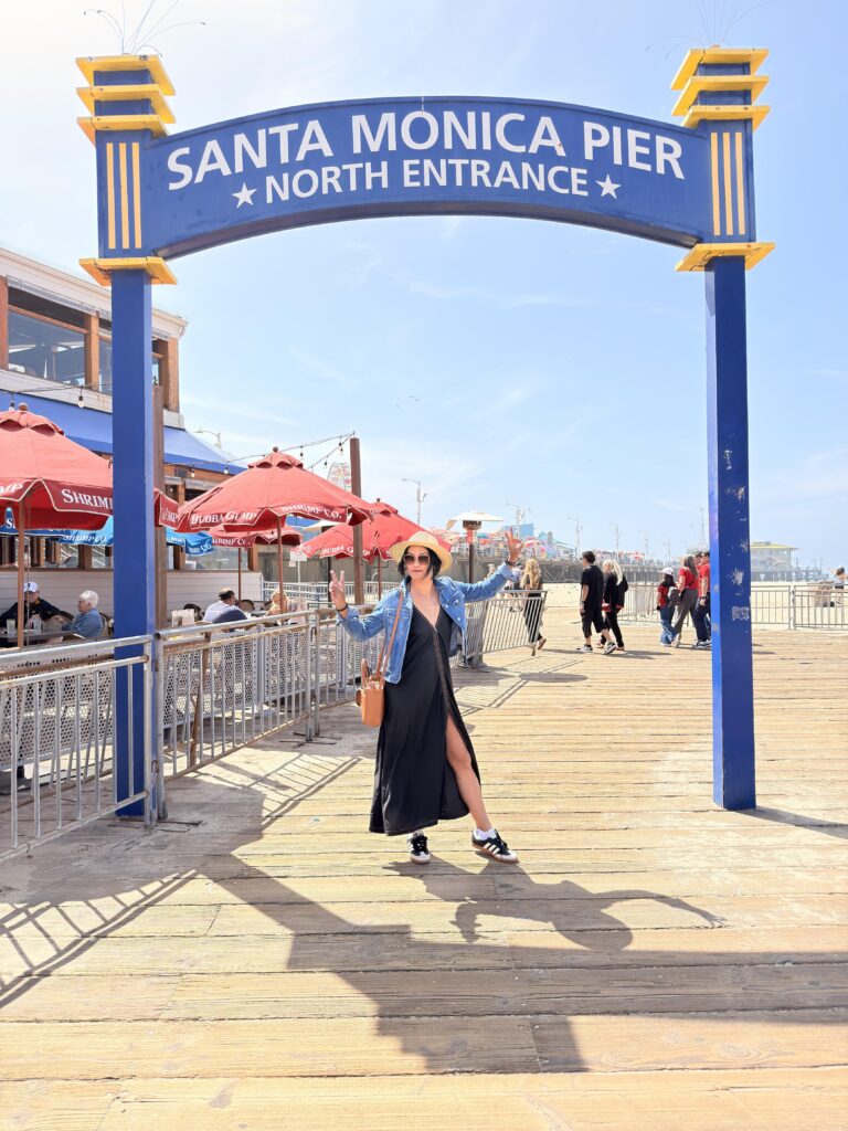 Frau macht Peace-Zeichen unter dem Schild "Santa Monica Pier North Entrance"