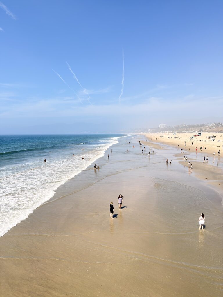 Luftaufnahme des Strandes von Santa Monica mit Spaziergängern im flachen Wasser und blauem Meer