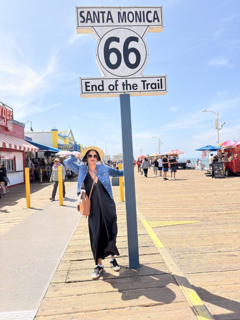 Frau posiert unter dem Schild "Santa Monica 66 End of the Trail" auf dem Pier