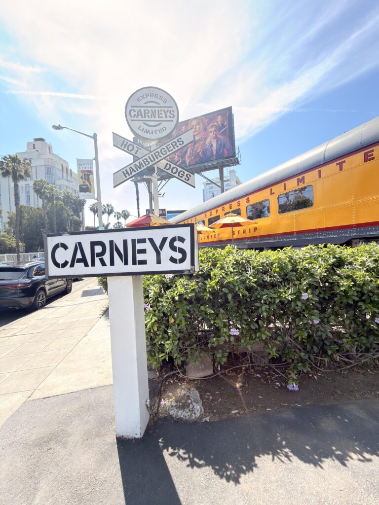 Schild "Carneys" vor einem gelben Eisenbahnwaggon-Diner mit Aufschrift "Hamburgers Hot Dogs" am Sunset Strip