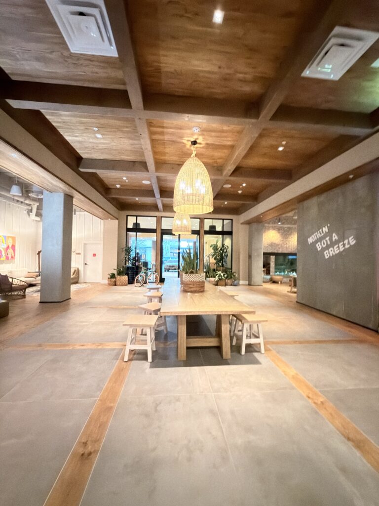 Lobby des Margaritaville Hotels San Diego mit Holzbalkendecke, langem Tisch und Schriftzug "Nothin' but a Breeze"