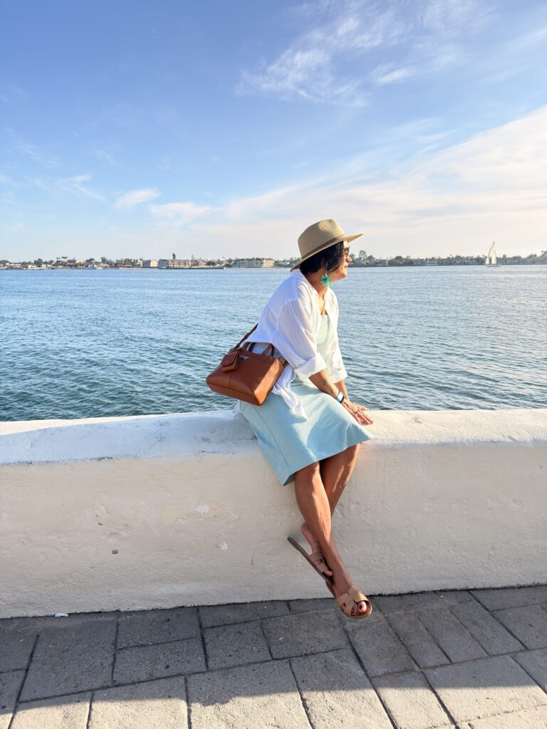 Frau mit Hut sitzt auf einer Mauer mit Blick auf die Bucht in Seaport Village San Diego