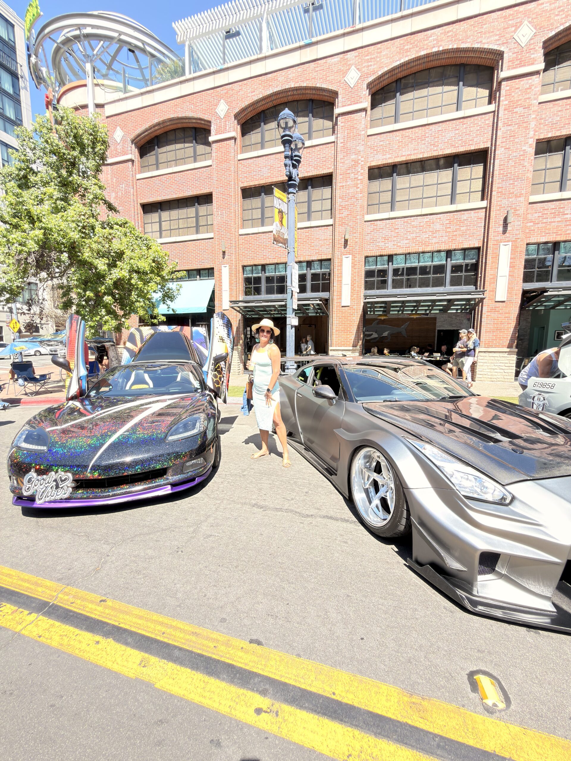 Frau steht zwischen zwei getunten Sportwagen bei der Cars-&-Coffee-Veranstaltung im Gaslamp Quarter San Diego