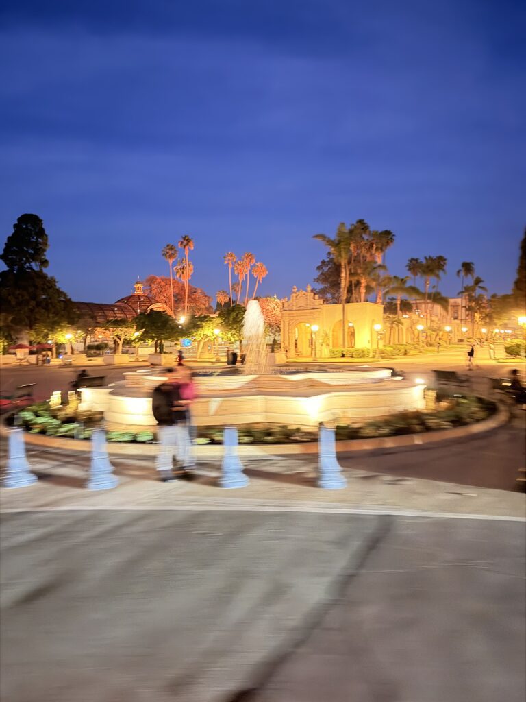 Beleuchteter Brunnen im Balboa Park San Diego bei Dämmerung, umgeben von Palmen und historischen Gebäuden im spanischen Kolonialstil