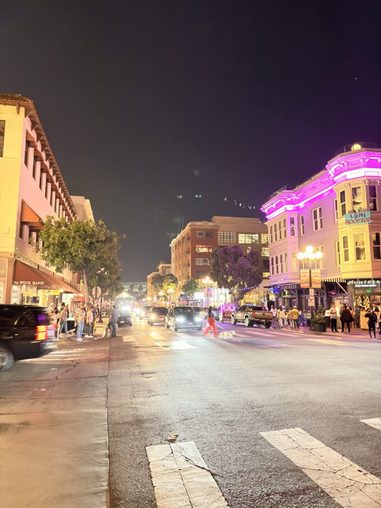 Beleuchtete Straße im Gaslamp Quarter San Diego bei Nacht mit pinkfarben angestrahlten Fassaden, Passanten und Autos