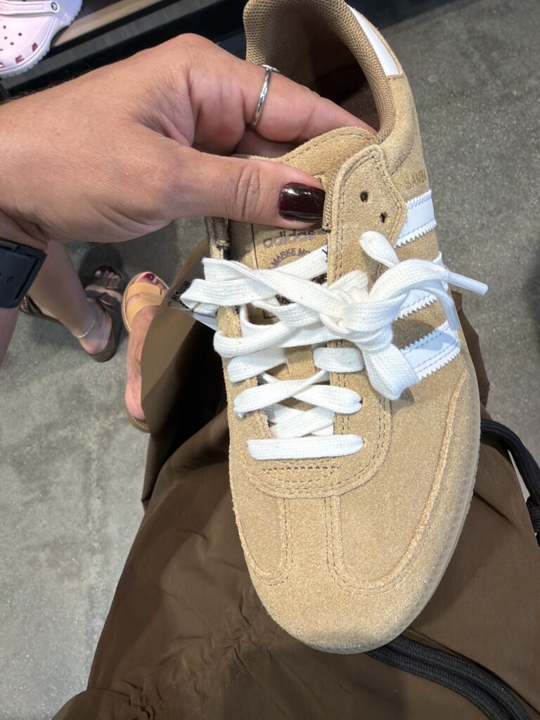 Hand hält einen beigen Adidas Samba Sneaker im Desert Hills Outlet